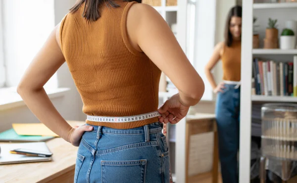 Девушка измеряет обхват талии у зеркала
